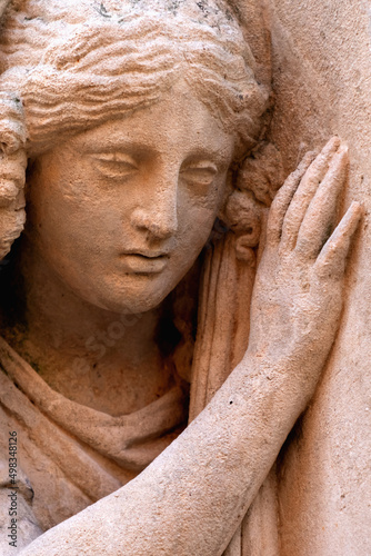 Close up fragment of an ancient statue of sad and desperate woman on tomb.