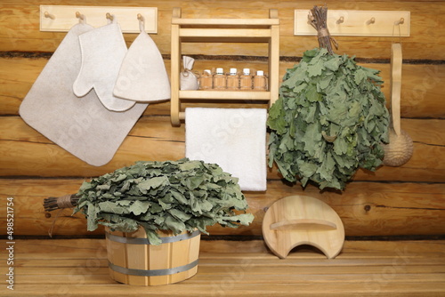 Traditional sauna accessories and oak brooms are in interior of log bath house. 