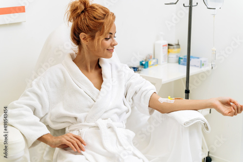 Woman sitting in armchair and closed eyes while receiving IV infusion with vitamins