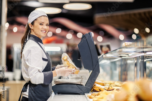 A happy bakery department saleswoman selling pastry at supermarket.