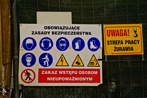 Tablica z obowiązującymi na budowie zasadami bezpieczeństwa w formie piktogramów . Tabliczka : " Uwaga strefa pracy żurawia " .