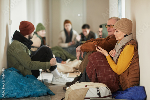 Side view portrait of Caucasian refugees sitting on floor in shelter covered with blankets