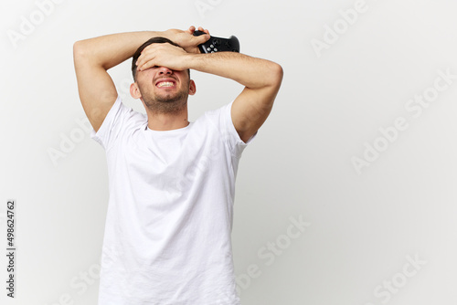 Screaming aggressive tanned handsome man in basic t-shirt failed in the game raise joystick gamepad up posing isolated on over white studio background. Copy space Banner Mockup. Gamer RPG concept