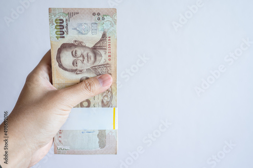 Someone hand holding a pile of one thousand Thai baht banknotes isolated on white background. The baht is the official currency of Thailand.