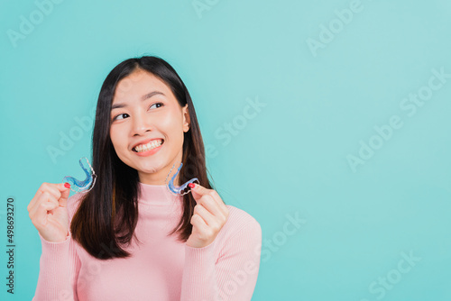 Portrait Asian beautiful young woman smiling hold silicone orthodontic retainers for teeth, Teeth retaining tools after removable braces, isolated blue background, Dental hygiene healthy care concept