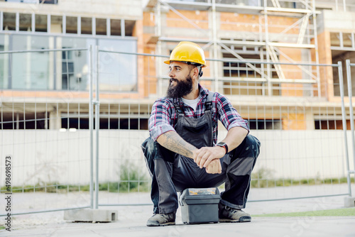 A worker sitting on a toolbox and waiting for a ride at construction site.