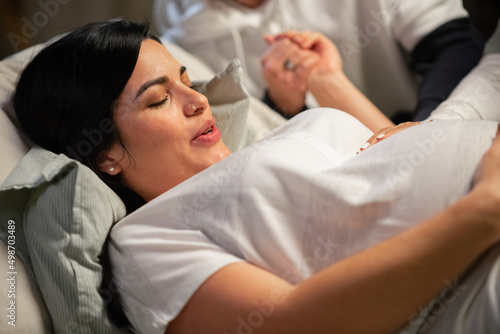 Dark-haired woman giving birth at home. Woman with pierced nose lying, feeling contractions during childbirth. Pregnancy, home birth concept