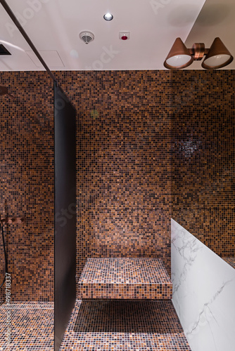 Elegancka, luksusowa i nowoczesna łazienka z prysznicem i deszczownicą. Ciekawie prezentująca się na ścianie mozaika o ciepłej barwie.