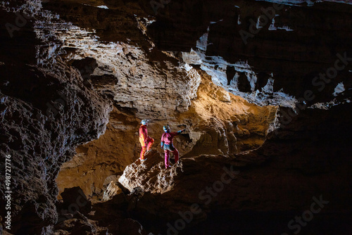 Two cavers - girl and boy are looking through the cave gallery; speleology