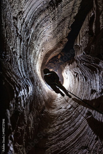 Man is climbing on the rope in the cave; caver or speleologist