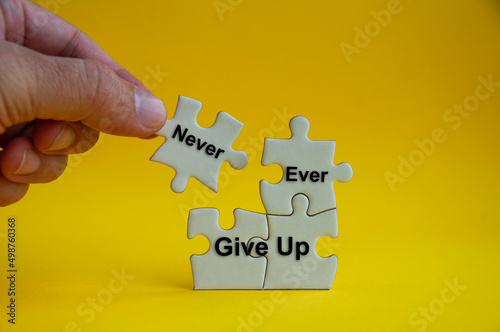 Motivational text on jigsaw puzzle with hand holding a missing jigsaw - Never ever give up.