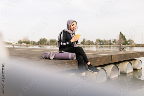 pretty woman in hijab sitting in the park looking at her mobile phone, woman in sportswear resting