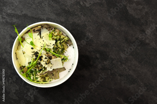 Risotto with mushrooms and parmesan in bowl on black background. Restaurant dish delivery. Top view. Free space for text. Healthy food concept.