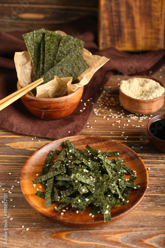 Plate and bowl of tasty seaweed sheets with sesame on wooden background