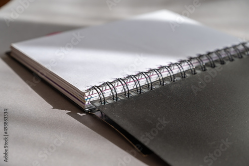 Black spring-loaded notebook against a gray background. Close-up of an open notebook and blank white sheets.