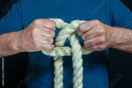 Hands of a man with effort untying a knot on a thick rope.