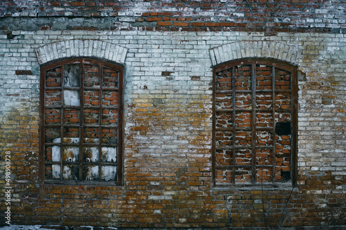 The wall of an old abandoned factory, the arched windows are bricked up, but the wooden frames remain, the brickwork was once painted, the paint has long since peeled off in places