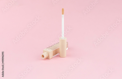 Cream concealer for correcting facial imperfections with an applicator on a pink background