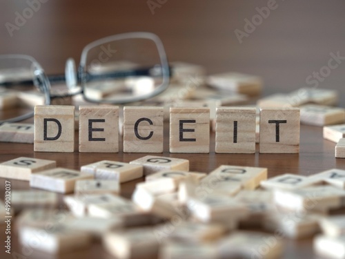 deceit word or concept represented by wooden letter tiles on a wooden table with glasses and a book