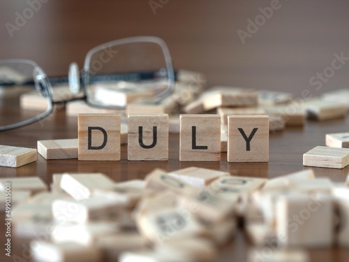 duly word or concept represented by wooden letter tiles on a wooden table with glasses and a book