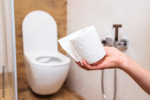 A woman's hand holds a roll of white toilet paper close-up. Bathroom background