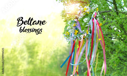 Beltane blessings. Flower wreath with colorful ribbons in garden, green natural background. floral decor, Symbol of Beltane, Wiccan Celtic Holiday beginning of summer. pagan witch traditions, rituals.