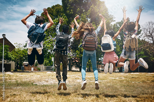 Schools out. Rearview shot of a group of unidentifiable schoolchildren jumping in the park.