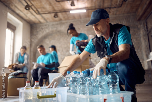 Mature volunteer organizing donations in boxes while working at humanitarian aid center.