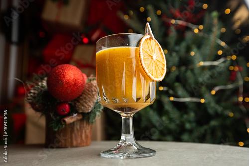 Shiny glass of hot orange grog cocktail served on counter in cafe on new year decoration background