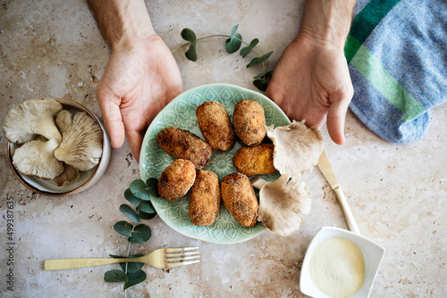 Someone holds a plate of mushroom croquettes on a marble table