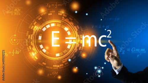 The teacher's hand points to the equation of relativity of Albert Einstein. E equals m multiplied by c squared. In the concept of a physics equation ring and a dark blue background. physics education.