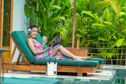 Asian tourists, Asian tourists, wearing dresses, lounging in the sun loungers by the pool, reading magazines during the summer vacation.