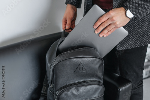 Man hand pulls a gray laptop with a black leather stylish backpack