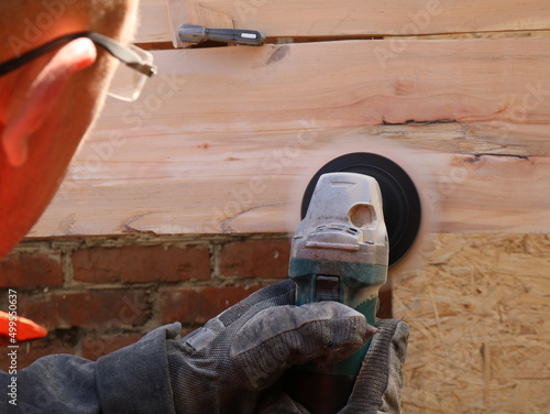 the movement of a round emery nozzle on a grinder in the hands of a man in glasses visible from the back in the process of smoothing the surface of a wooden texture board