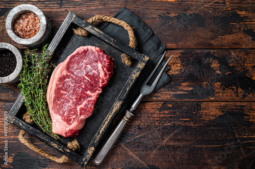 Prime raw new york beef meat steak with herbs ready for cooking. Wooden background. Top view. Copy space