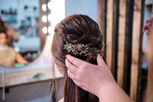 Stylist making a hairstyle to female client with a stylish hair accessory at the beauty salon.