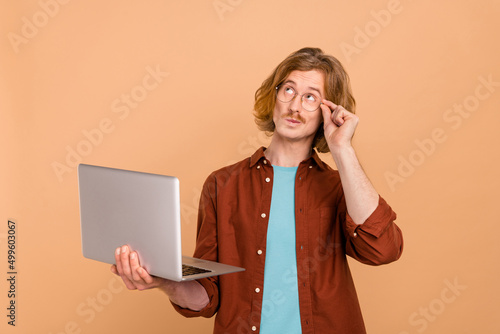 Portrait of handsome minded trendy red-haired guy using laptop deciding isolated over beige pastel color background