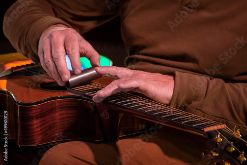 Guitariste jouant sur sa guitare folk posée à plat avec un bottleneck en fer. Gros plan réalisé pendant un concert.