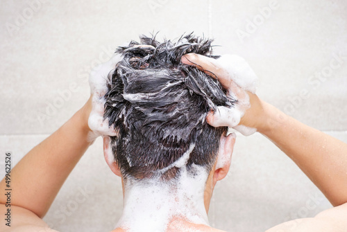 Male hand washes his head with shampoo and foam on gray background close-up, back view.