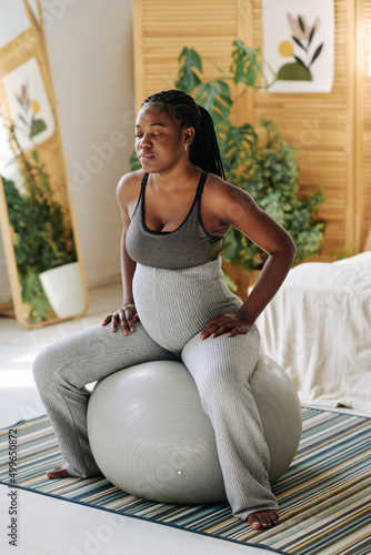 Pregnant girl sitting on fitness ball and concentrating with her eyes closed during contractions