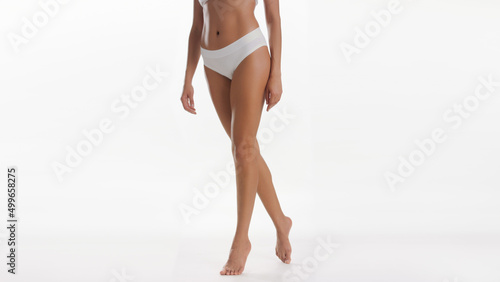 Woman's legs. Medium long shot of slim African American woman in white underwear standing on tiptoes against white background | Smooth legs and leg care concept