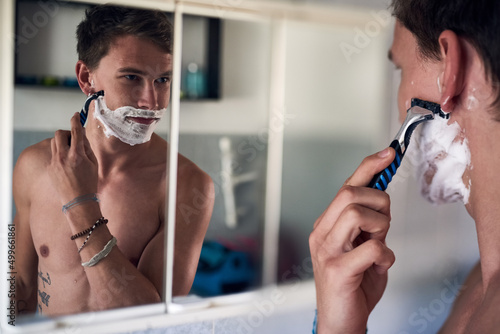 Good morning handsome. Shot of a young man shaving his beard while looking at himself in the mirror.