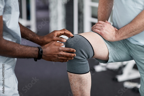 Close up of African American therapist examining senior man with knee injury in rehabilitation clinic