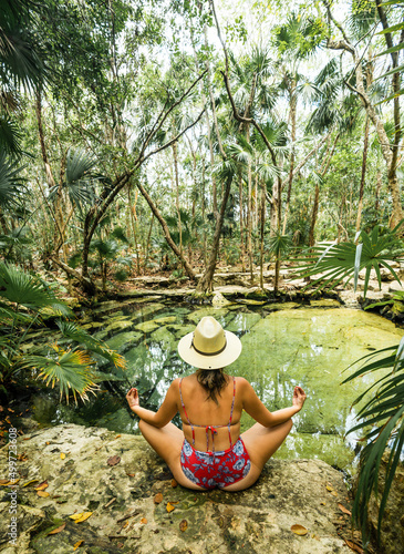 young hispanic woman with hat meditates in a cenote in the jungle of mexico