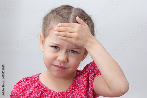 Child with headache holding hand on forehead on white background caucasian little girl 5-6 years in red looking at camera