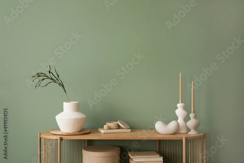 Stylish living room interior design wooden chest of drawers, beige vase and creative home accessories. Sage green wall. Copy space. Template.