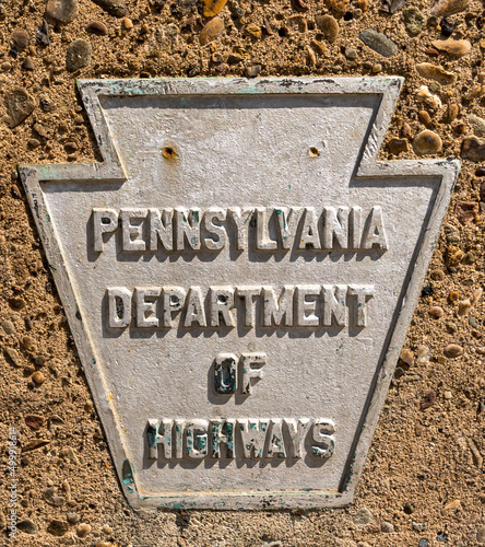 A metal sign in the shape of a keystone with Pennsylvania Department of Highways on it shown on a concrete wall. The plaque signified property owned and maintained by that department