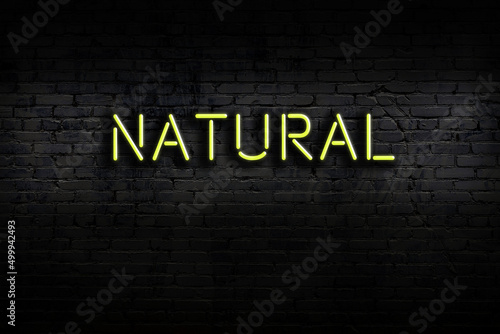 Night view of neon sign on brick wall with inscription natural