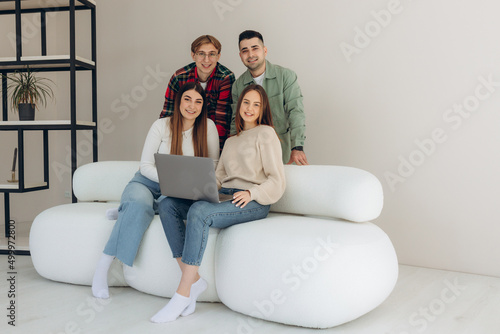 Group of diverse friends sitting on sofa watching videos online or using social networking app on laptop