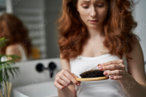 Redhead shocked caucasian woman holding hairbrush with lost hair